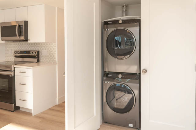 Bright kitchen with white cabinetry and stainless steel appliances, featuring a modern laundry area with stacked washer...