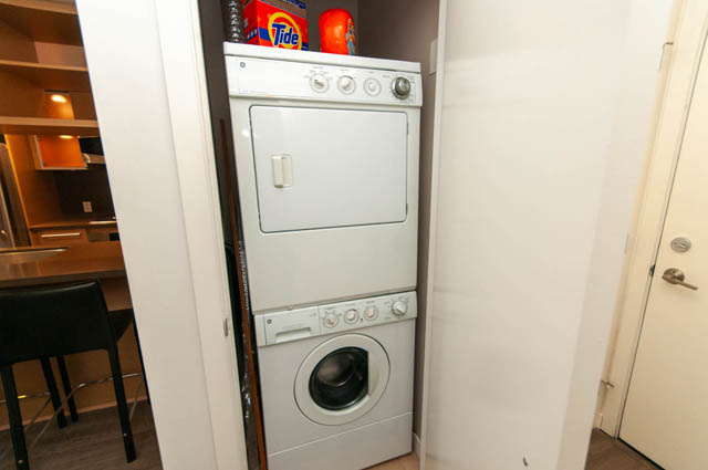 Bright laundry room with stacked washer and dryer, counter space, and door access. - 1102-833 Seymour Street, Vancouver Downtown