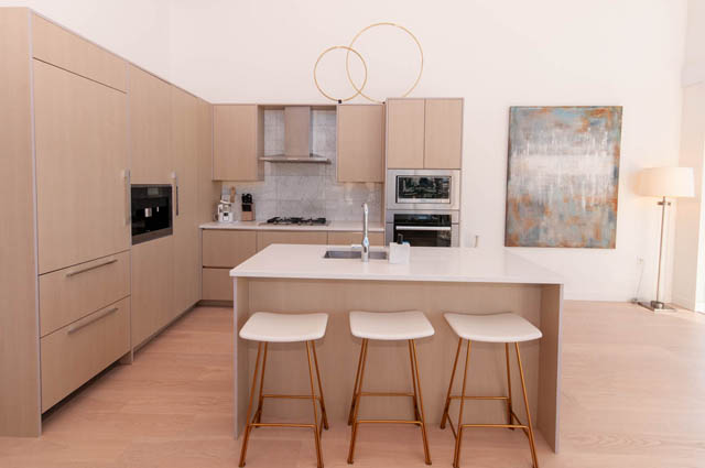 Modern kitchen with light wood cabinets, white countertops, and gold bar stools. - 2818  - 89 Nelson Street, Vancouver Downtown