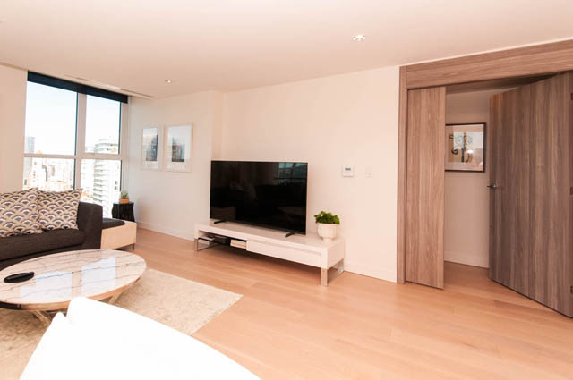 Spacious penthouse living room with hardwood floors, a sleek TV setup, and a city view from the large window.