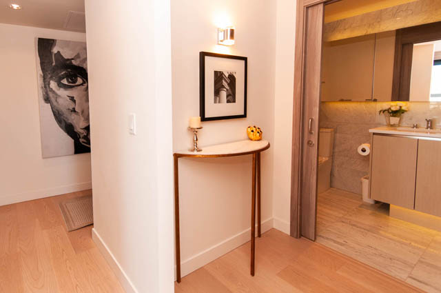 Elegant entryway with marble console table, framed art, and hardwood floors leading to a modern bathroom.