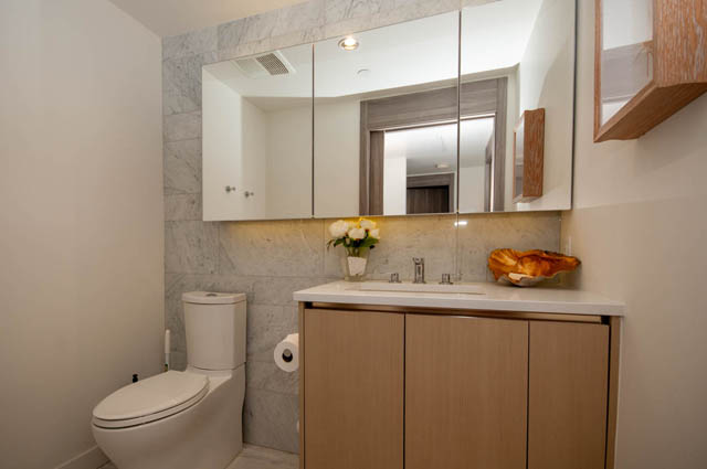 Modern bathroom with marble countertops and a wooden vanity, featuring a sleek sink and a vase of flowers.