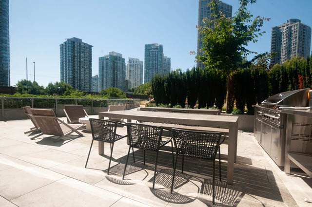 Spacious rooftop patio with a city view, featuring a large wooden table, comfortable seating, and a built-in grill.