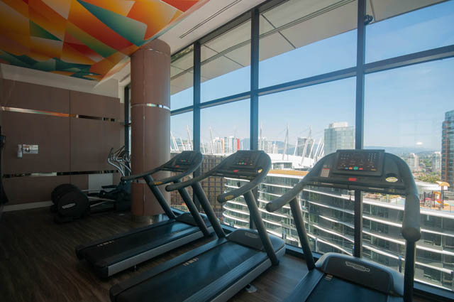 Spacious penthouse with hardwood floors, large windows offering a stunning city view, and modern fitness equipment.