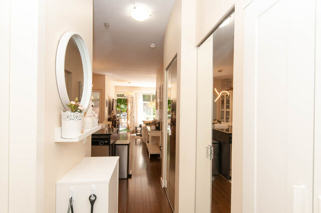 Bright entry hallway with hardwood floors, a round white mirror, and mirrored closet doors. - 102-1633 Mackay Avenue, North Vancouver