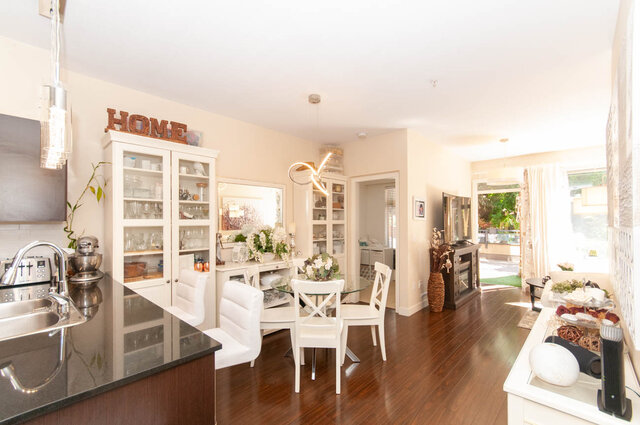 Bright open kitchen and dining area with dark granite countertops, white bar stools, and polished hardwood floors.