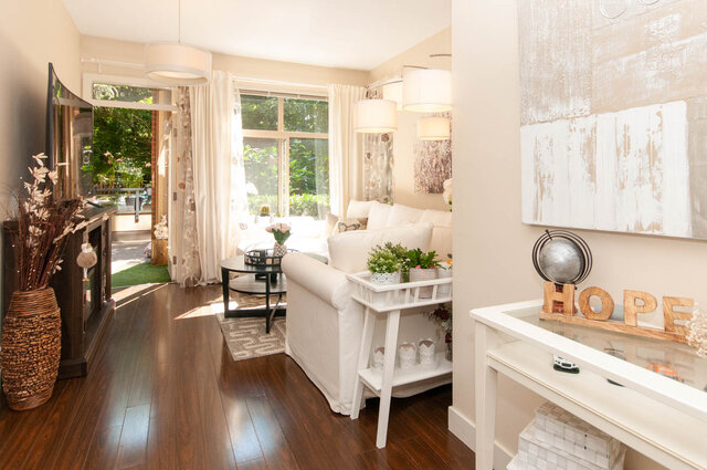 Bright living room with white slipcovered sofa, dark hardwood floors, and a glass door opening to a green balcony.