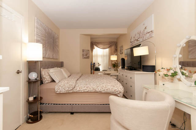 Spacious bedroom with white furniture, floral bedding, and a large vanity mirror. - 102-1633 Mackay Avenue, North Vancouver