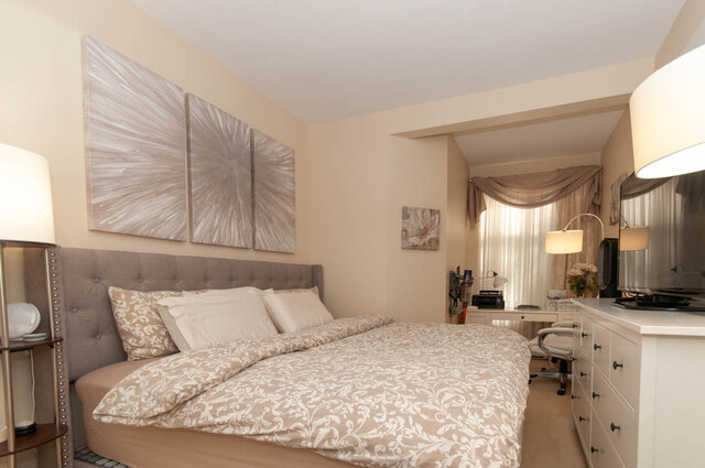 Furnished bedroom with tufted headboard, damask bedding, and abstract triptych art above the bed. - 102-1633 Mackay Avenue, North Vancouver