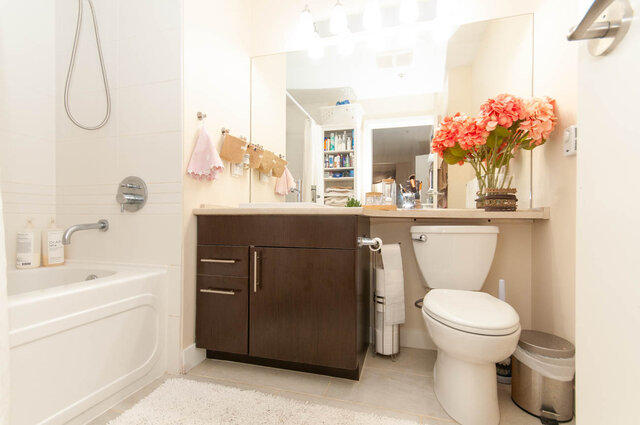 Clean bathroom with a dark wood vanity, white tub, and a vase of coral hydrangeas on the counter. - 102-1633 Mackay Avenue, North Vancouver