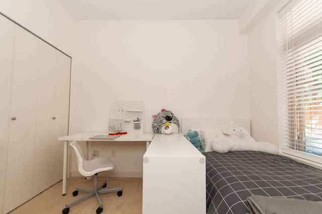 Spacious bedroom with a desk, white walls, and a cozy bed with a checkered blanket. - 102-1633 Mackay Avenue, North Vancouver
