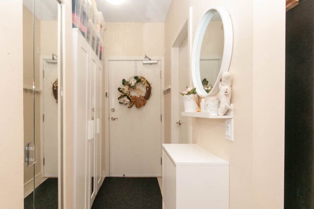 Bright entryway hallway with white cabinetry, a round wall mirror, and a floral wreath on the door. - 102-1633 Mackay Avenue, North Vancouver