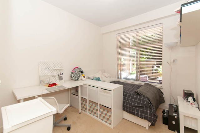 Bright bedroom with white desk, checkered bedding, and large window with blinds. - 102-1633 Mackay Avenue, North Vancouver