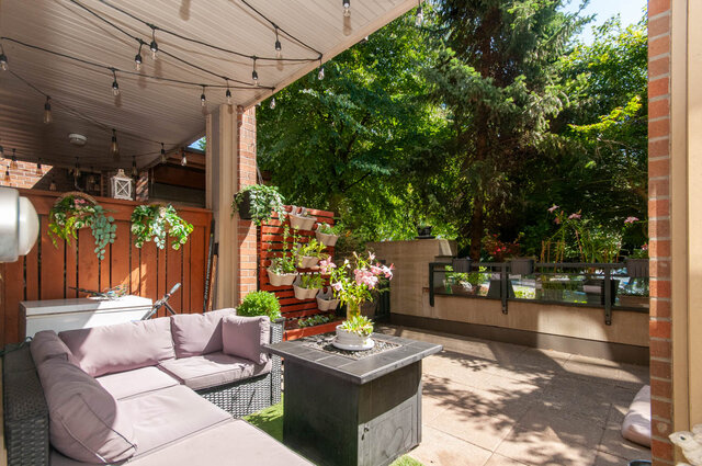 Covered patio with wicker sectional, mauve cushions, string lights, and a vertical planter wall. - 102-1633 Mackay Avenue, North Vancouver