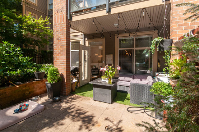Furnished patio with wicker seating, string lights, and potted plants beside a brick column. - 102-1633 Mackay Avenue, North Vancouver
