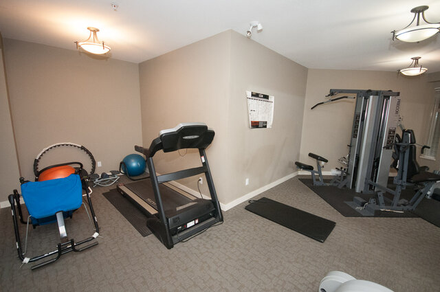 Compact home gym with a treadmill, weight machines, and exercise balls on neutral carpeted flooring. - 102-1633 Mackay Avenue, North Vancouver