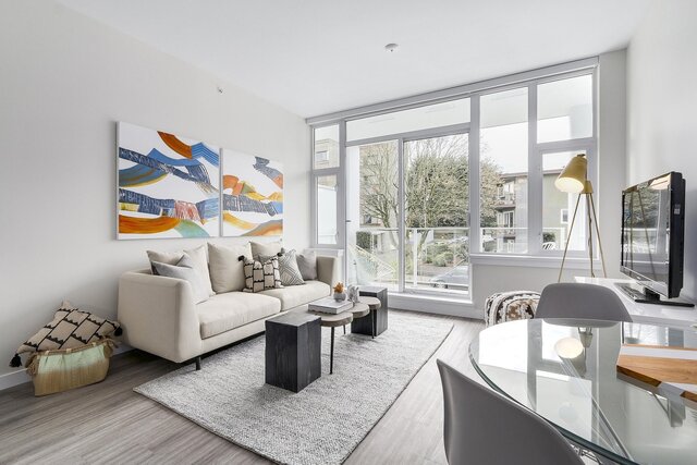 The living room features a sofa, coffee tables, artwork on the wall, large windows, a TV, and hardwood floors.