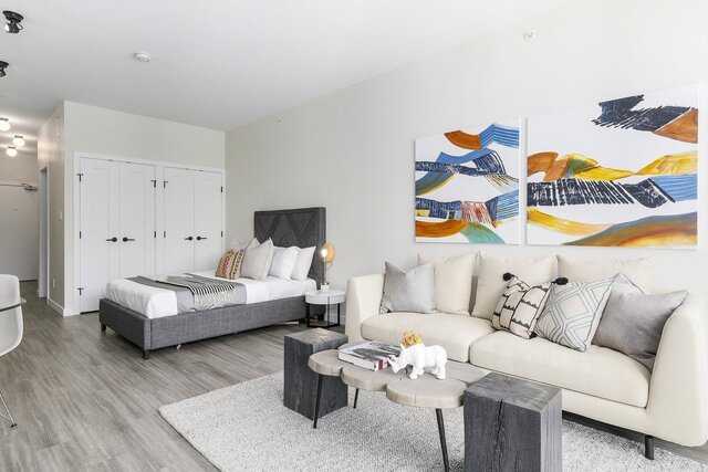 The bedroom has a bed with pillows and a striped blanket, a sofa with decorative cushions, a coffee table on an area rug, two