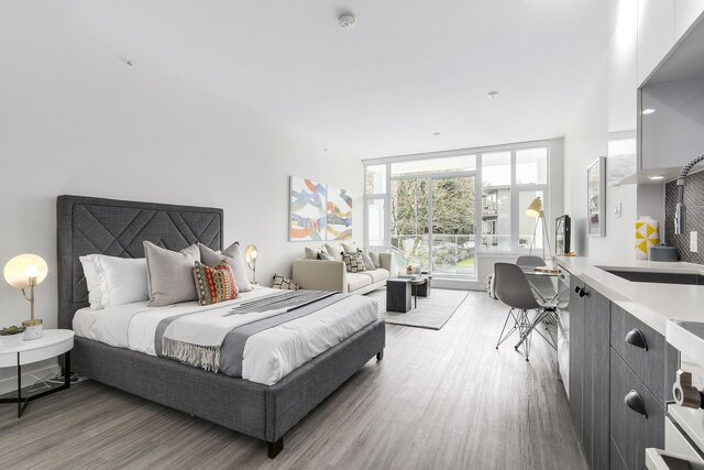 This bedroom features a bed, sofa, kitchenette, large windows, and hardwood floors. - 212-311 East 6th Avenue, Vancouver East Side