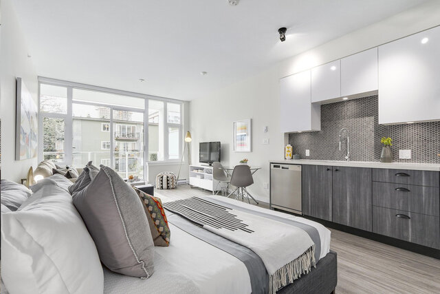 A bedroom with a bed, large windows, kitchen cabinets, dining table, and light wood flooring. - 212-311 East 6th Avenue, Vancouver East Side
