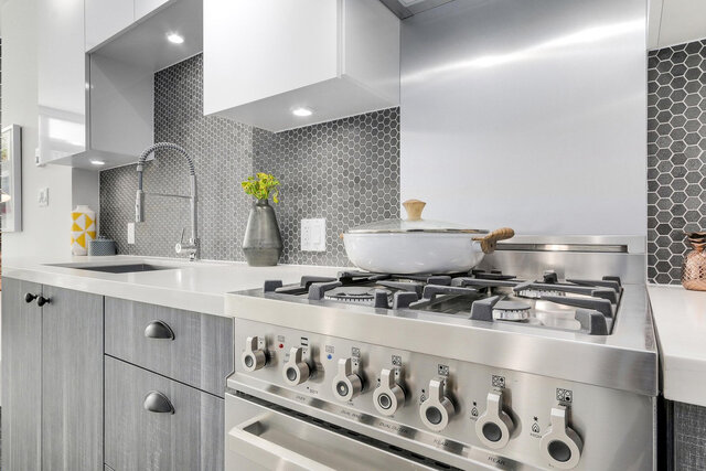kitchen featuring a stainless steel gas stove, white countertops, gray hexagonal tile backsplash, and under-cabinet lighting