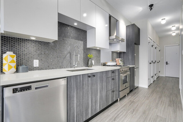 The kitchen features white countertops, gray cabinets, stainless steel appliances, a hexagonal tile backsplash, and a sink.
