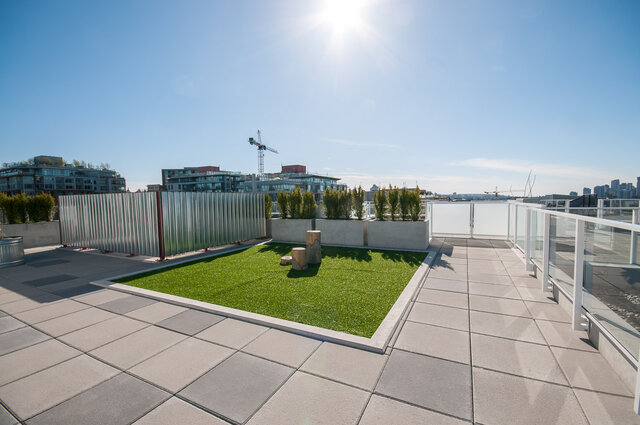 The balcony has a grass area, planters with shrubs, glass railings, and a city view. - 212-311 East 6th Avenue, Vancouver East Side