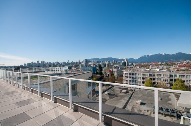 The balcony features tiled flooring, white railings, and a view of the city skyline and mountains. - 212-311 East 6th Avenue, Vancouver East Side