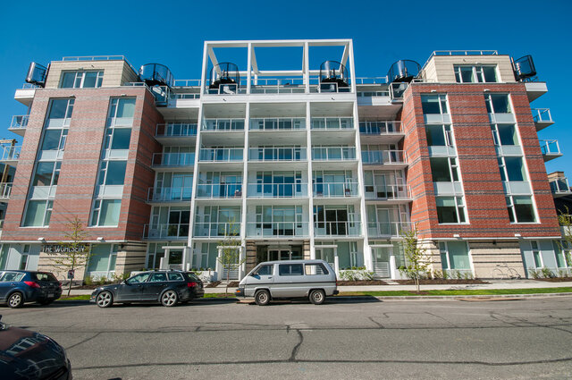 The building exterior shows a multi-story residential structure with brick and white structural elements, large windows, and 
