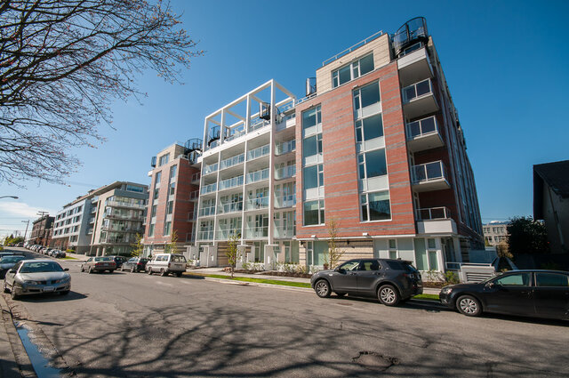 The building exterior shows a multi-story residential structure with brick and white facade, large windows, and balconies.