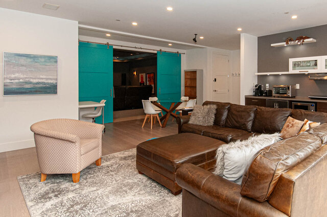 Spacious living room with leather couch, modern decor, and sliding teal doors leading to a dining area. - Suite - 392 Moyne Dr, West Vancouver