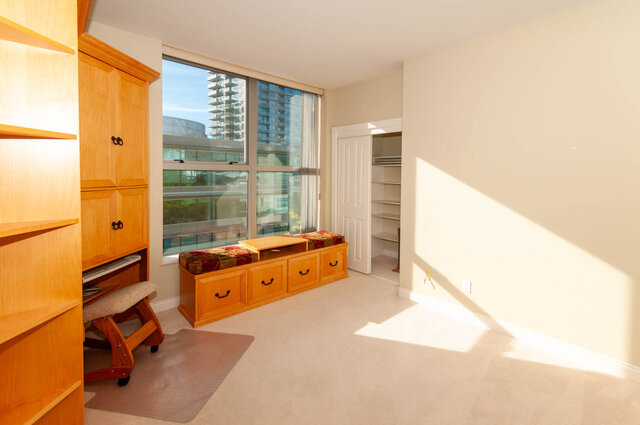 Bedroom with city view through large windows and light wood storage bench. - 607-160 E 13th Street, North Vancouver