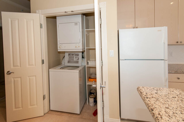 Laundry area with stacked washer/dryer and white refrigerator. - 607-160 E 13th Street, North Vancouver