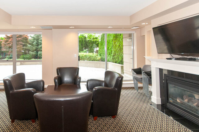 Cozy living room with dark leather seating and large windows overlooking greenery. - 607-160 E 13th Street, North Vancouver