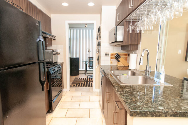 Modern kitchen with granite countertops and dark wood cabinets, featuring a stainless steel sink and a view of the living...