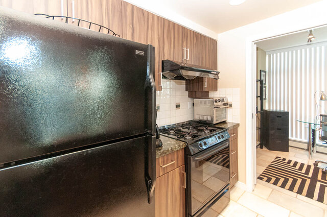 Bright kitchen with black countertops, stainless steel appliances, and wooden cabinets. - 905 - 1199 Marinaside Cres., Vancouver Downtown