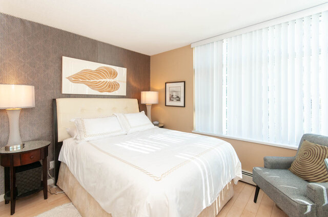Spacious bedroom with a king-sized bed, white bedding, and a large window with vertical blinds. - 905 - 1199 Marinaside Cres., Vancouver Downtown