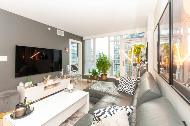 Spacious living room with a large window offering a city view, modern furniture, and a sleek TV setup. - 1006 -1618 Quebec Street, Vancouver East Side