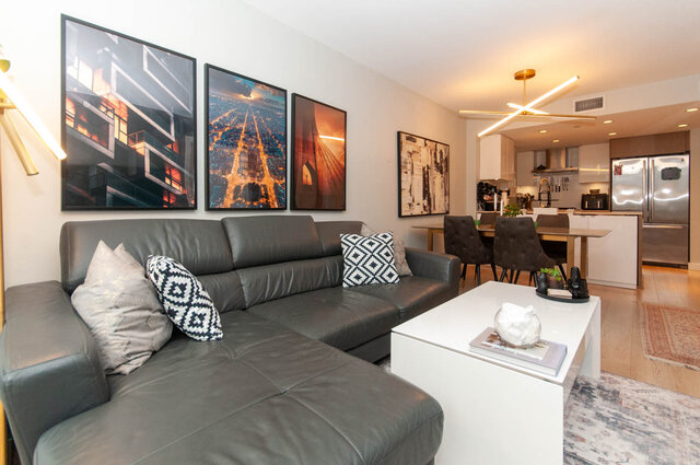 Spacious living room with modern leather sectional, large cityscape art, and sleek kitchen island. - 1006 -1618 Quebec Street, Vancouver East Side