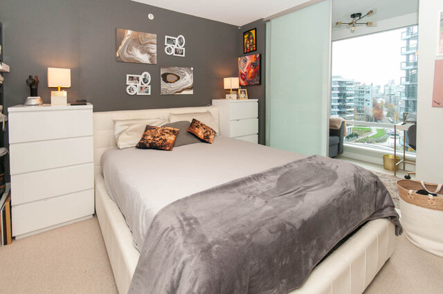 Spacious 1-bedroom + den condo with a cozy bedroom featuring a large bed, modern artwork, and a city view from the balcony.