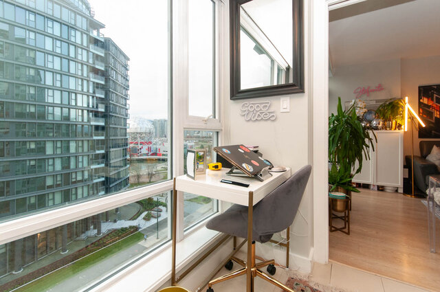 Bright and airy den with a city view, featuring a sleek white desk, gold accents, and a cozy corner with plants and a...