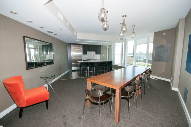 Modern dining area with a large wooden table, orange chairs, and a city view through large windows. - 1006 -1618 Quebec Street, Vancouver East Side