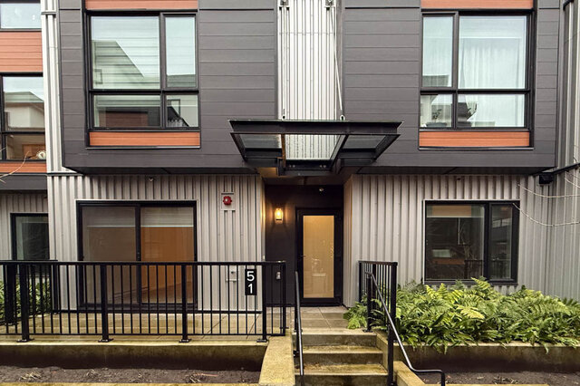 The entrance features a glass canopy, black metal railings, steps leading to a door with large windows above.
