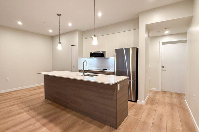 The kitchen features a central island with a sink, stainless steel refrigerator, cabinetry, pendant lighting, and hardwood fl