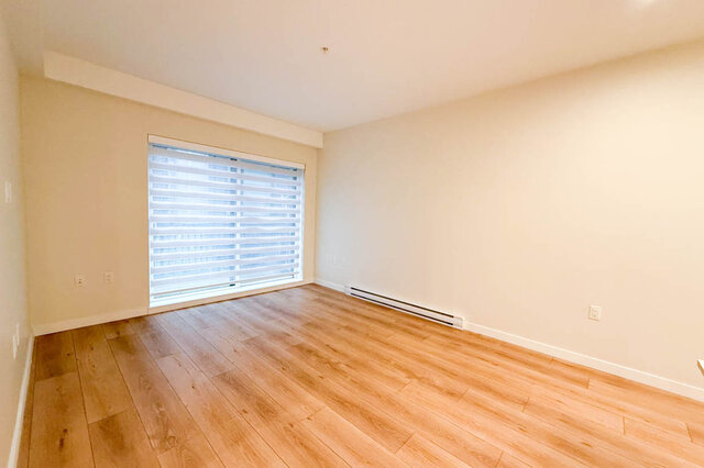 This bedroom has hardwood floors, a window with blinds, and a baseboard heater. - G 3- 2030 East 20th Ave, Vancouver East Side