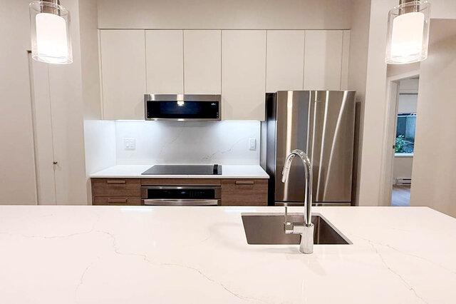 The kitchen has stainless steel appliances, white quartz countertops, under-cabinet lighting, and light-colored cabinets.