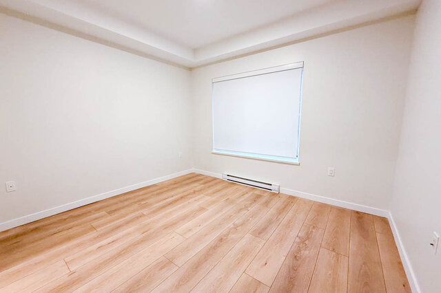 This is a bedroom with hardwood floors, a window with a blind, and a baseboard heater. - G 3- 2030 East 20th Ave, Vancouver East Side