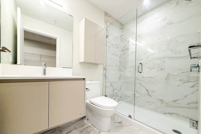 This bathroom contains a vanity with sink, toilet, glass shower enclosure, and marble tile walls and flooring.