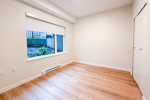 This bedroom has hardwood floors, a window with a roller shade, and a baseboard heater. - G 3- 2030 East 20th Ave, Vancouver East Side