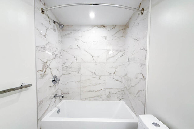 Bathroom with white marble tile walls, bathtub, showerhead, curved shower rod, and toilet - G 3- 2030 East 20th Ave, Vancouver East Side
